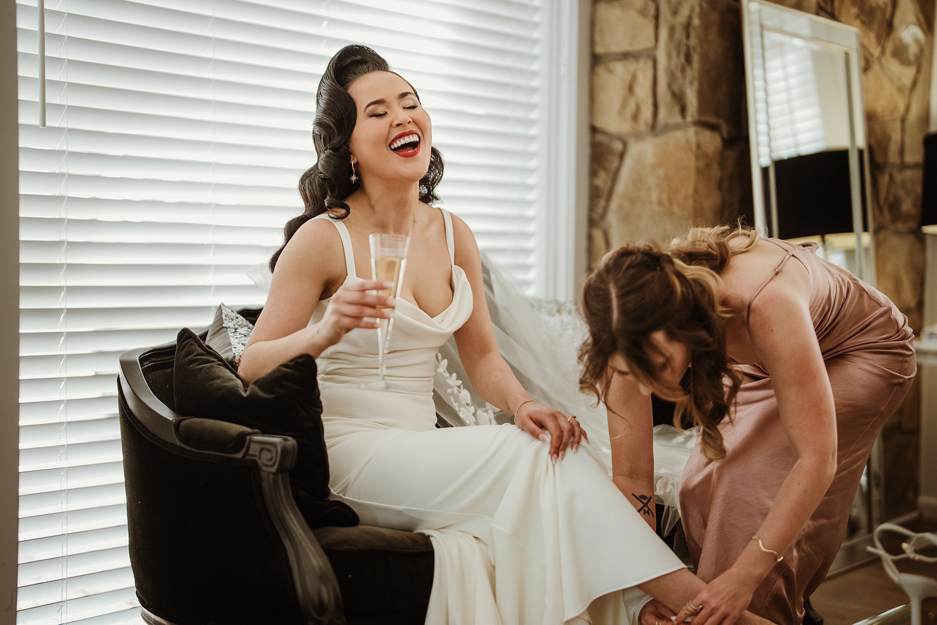 Bride laughing while enjoying a glass of champagne in the Bridal Retreat at Scotchmans Hill before her wedding ceremony.