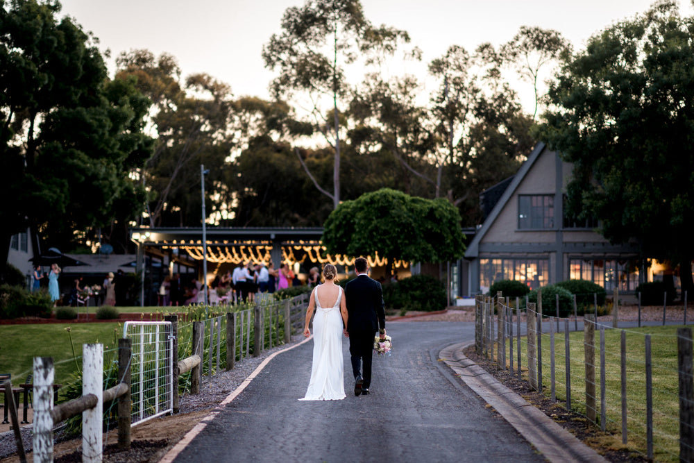 Newlywed couple walking toward their wedding reception at Scotchmans Hill winery near Geelong, under evening lights.