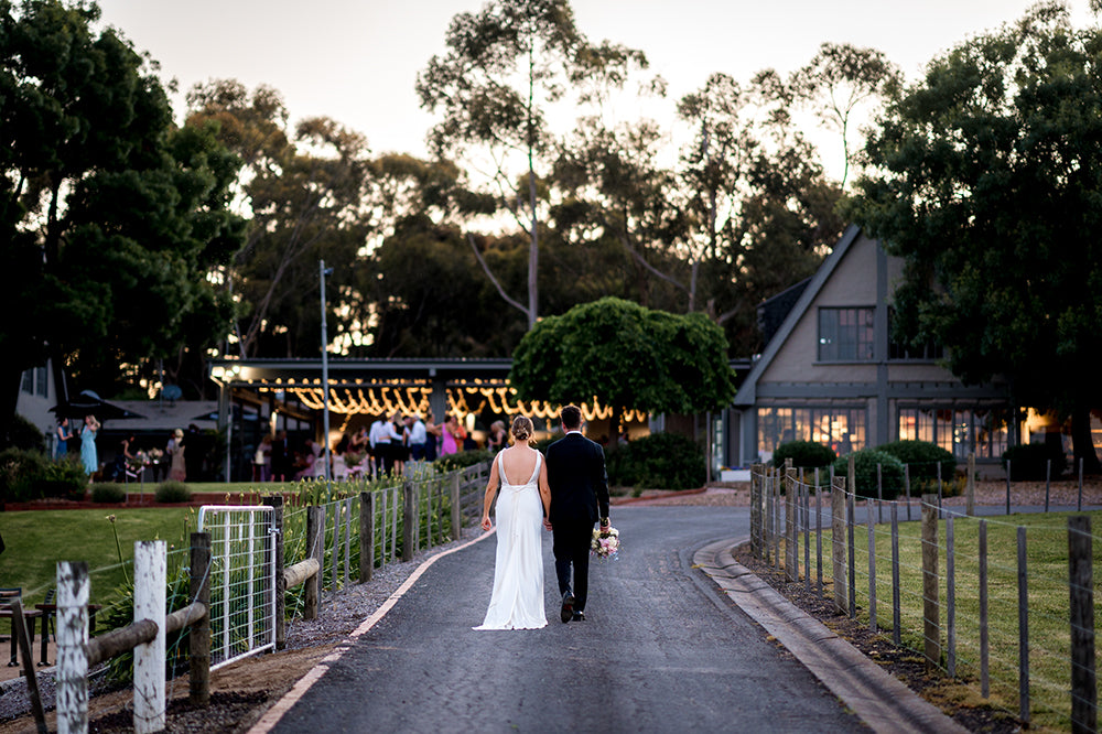 Bride and groom walking hand in hand towards the restaurant at Scotchmans Hill Bellarine Peninsula at dusk.