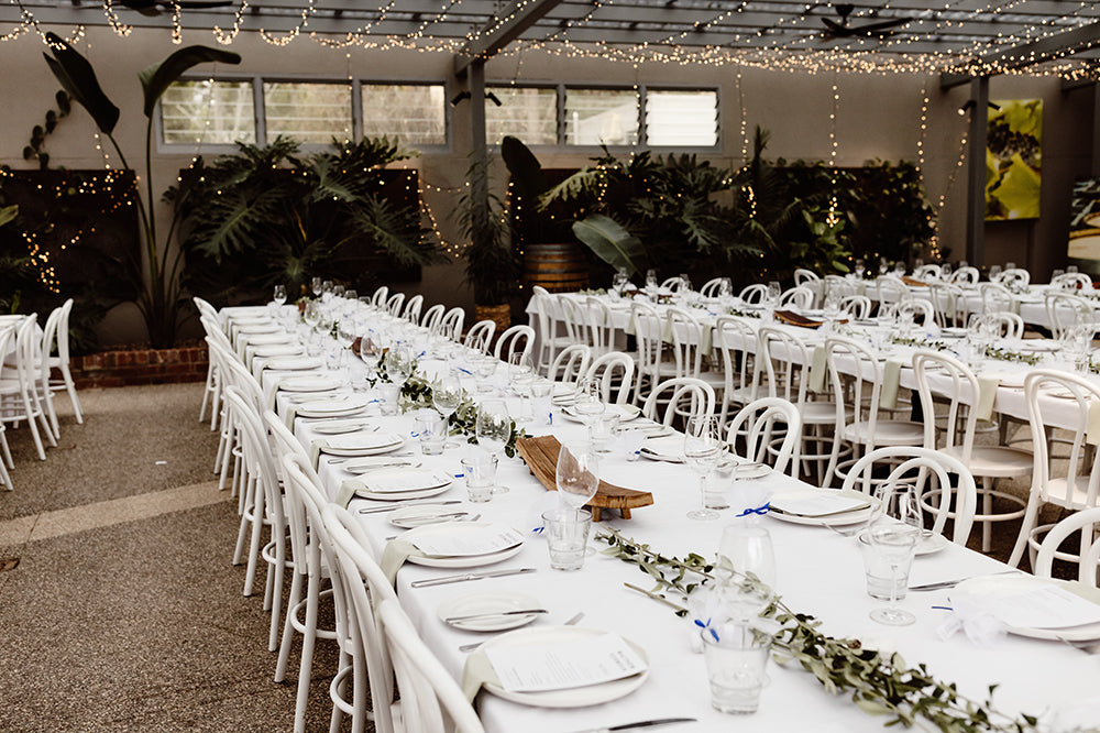 Wedding reception tables decorated with greenery and white tableware under string lights at Scotchmans Hill.