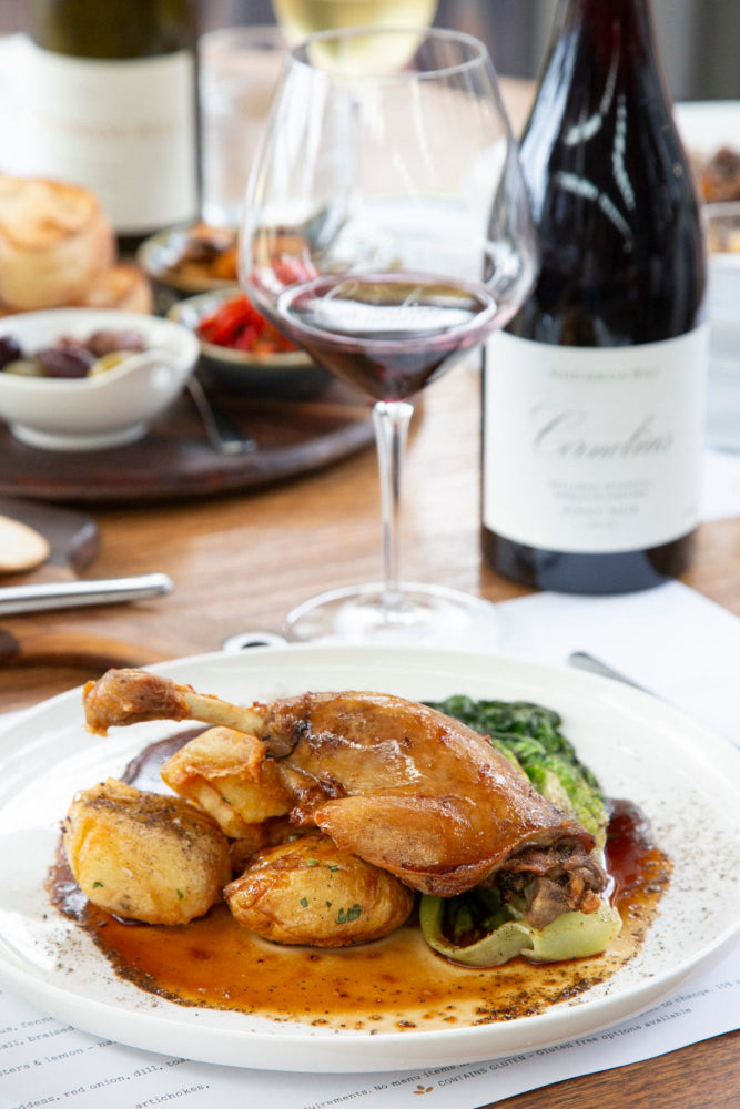 Dinner table with roasted duck, vegetables, and a bottle of wine.