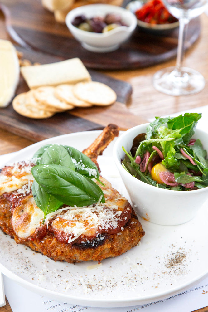 Plated dish with breaded meat, salad, and basil leaves on a wooden table.