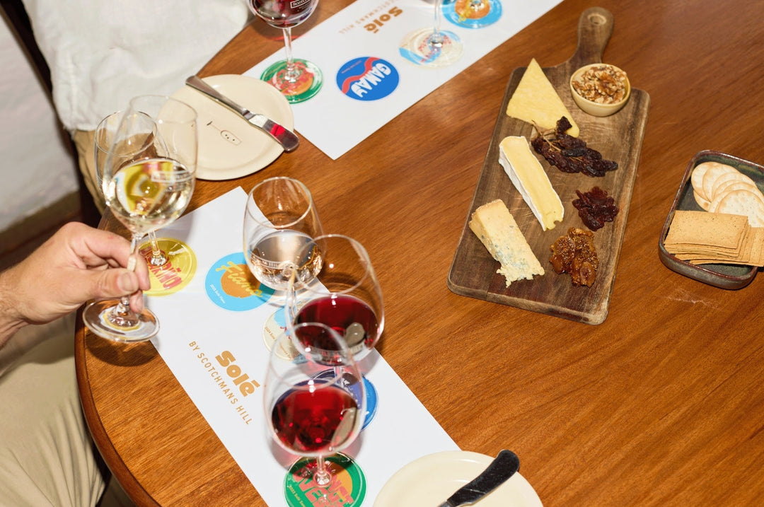 Solé wine tasting at Scotchmans Hill with glasses of Albariño, Fiano, Rosé, Gamay and Sangiovese, paired with artisan cheeses, crackers and dried fruits on a wooden table.